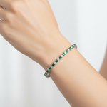 14k gold diamond and emerald tennis bracelet featuring round diamonds and emeralds on a model's wrist.