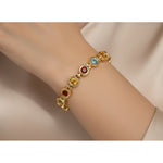 Gold bracelet with colorful gemstones on a wrist against a neutral background