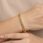 Gold bracelet with multicolored gemstones on a wrist against a beige background