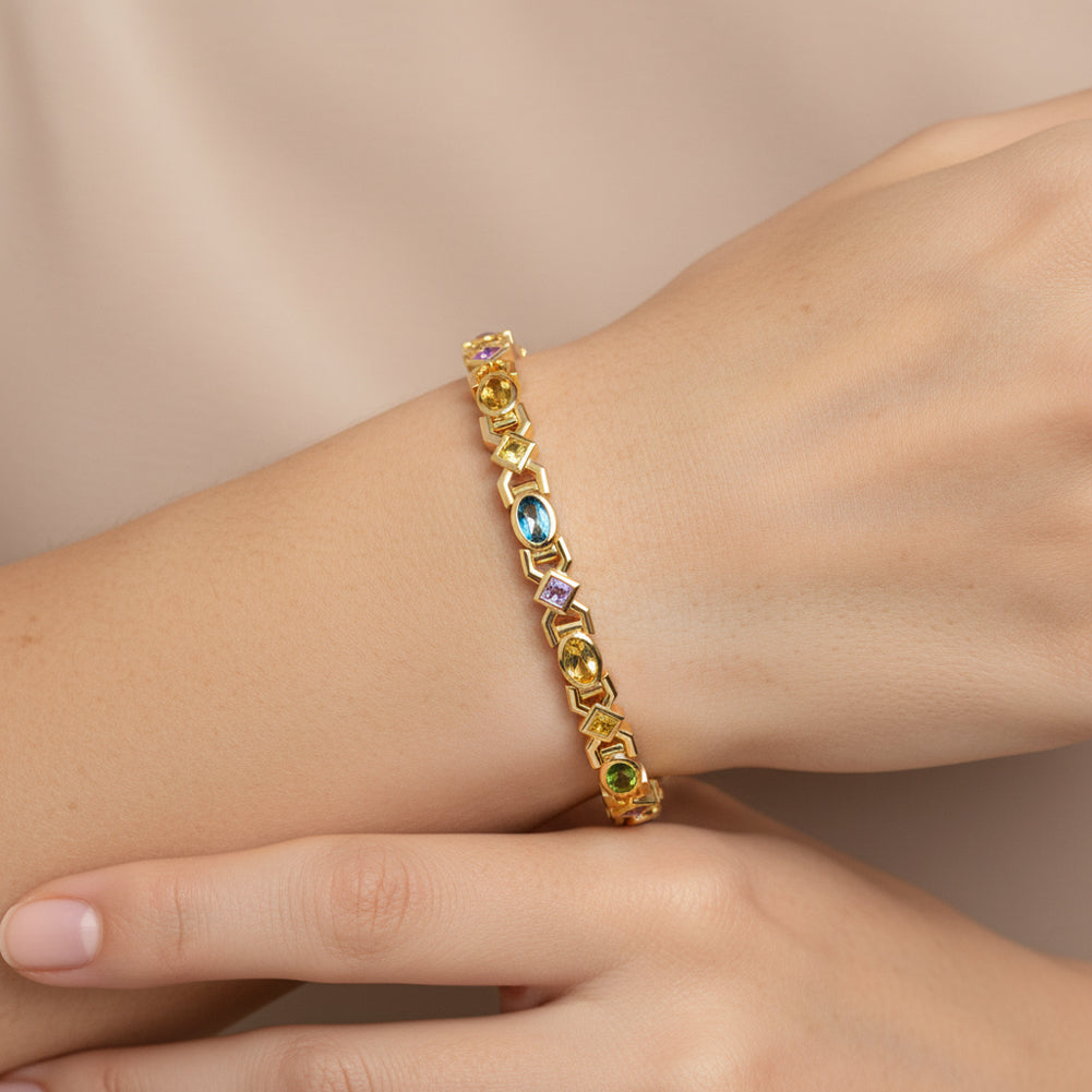 Gold bracelet with multicolored gemstones on a wrist against a beige background