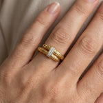Gold ring with a diamond on a person's finger against a neutral background