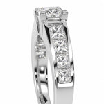 A close-up studio shot of a white gold or platinum ring featuring a princess-cut diamond center stone and a channel setting of smaller princess-cut diamonds along the band, set against a plain white background.