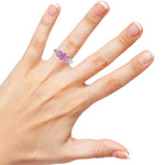 Hand wearing a ring with pink gemstones on a white background