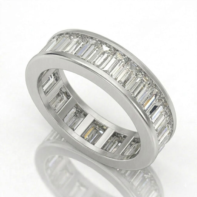 A white-colored eternity ring featuring a channel setting of baguette-cut clear stones on one side and round-cut stones on the other, displayed on a reflective white surface.